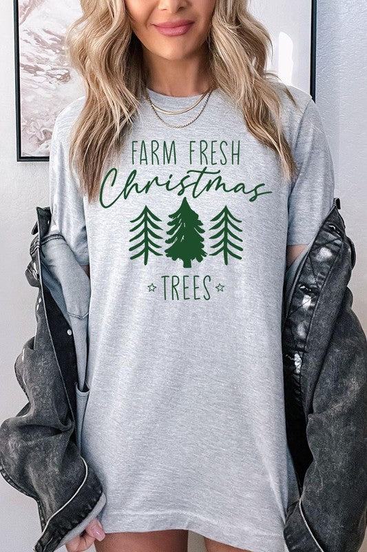 A woman wearing the "Farm Fresh Christmas Trees Graphic Tee" in green, adorned with white text and tree graphics.