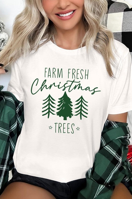 A woman wearing the "Farm Fresh Christmas Trees Graphic Tee" in green, adorned with white text and tree graphics.