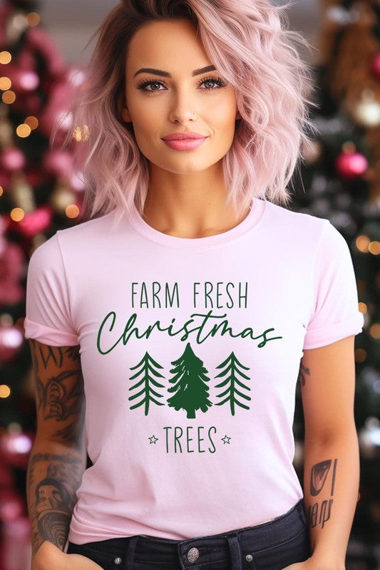 A woman wearing the "Farm Fresh Christmas Trees Graphic Tee" in green, adorned with white text and tree graphics.