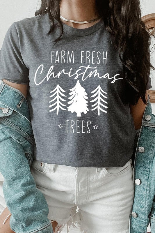 A woman wearing the "Farm Fresh Christmas Trees Graphic Tee" in green, adorned with white text and tree graphics.