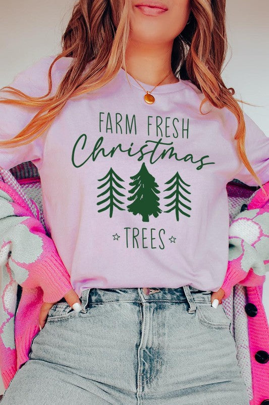 A woman wearing the "Farm Fresh Christmas Trees Graphic Tee" in green, adorned with white text and tree graphics.