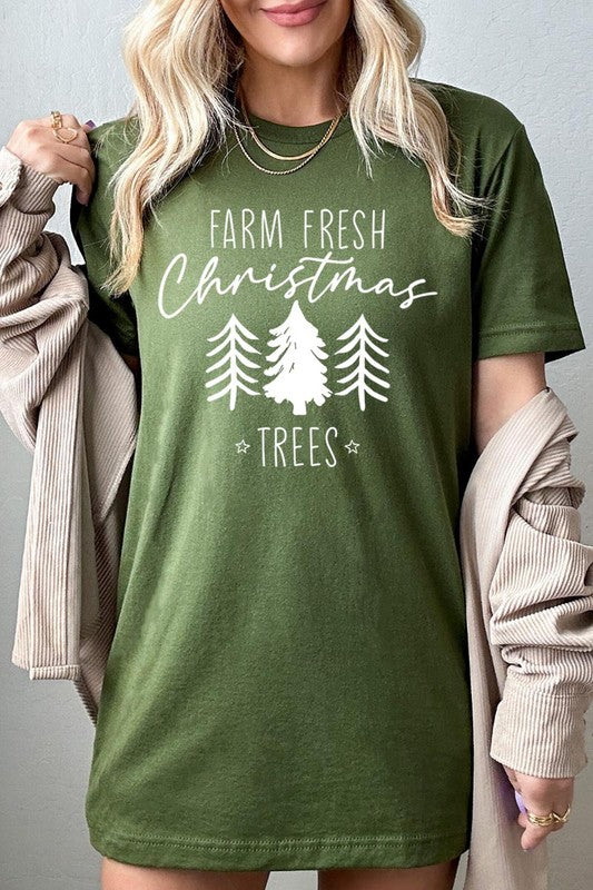 A woman wearing the "Farm Fresh Christmas Trees Graphic Tee" in green, adorned with white text and tree graphics.