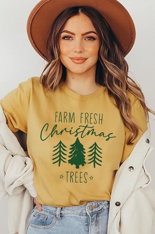 A woman wearing the "Farm Fresh Christmas Trees Graphic Tee" in green, adorned with white text and tree graphics.