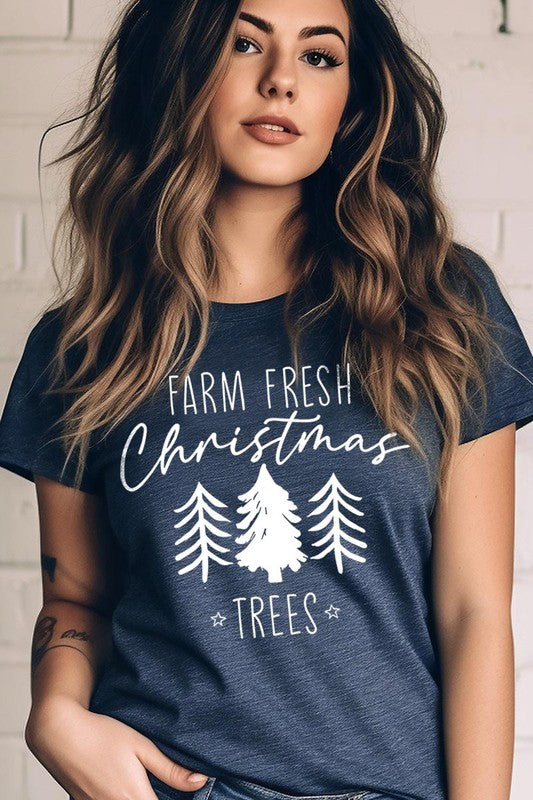 A woman wearing the "Farm Fresh Christmas Trees Graphic Tee" in green, adorned with white text and tree graphics.