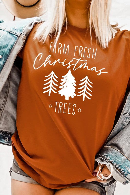 A woman wearing the "Farm Fresh Christmas Trees Graphic Tee" in green, adorned with white text and tree graphics.