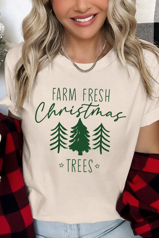 A woman wearing the "Farm Fresh Christmas Trees Graphic Tee" in green, adorned with white text and tree graphics.