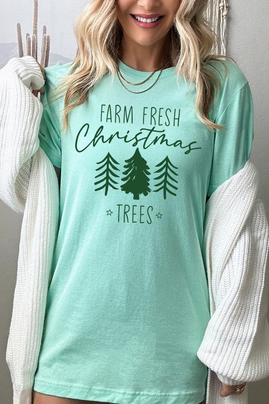 A woman wearing the "Farm Fresh Christmas Trees Graphic Tee" in green, adorned with white text and tree graphics.