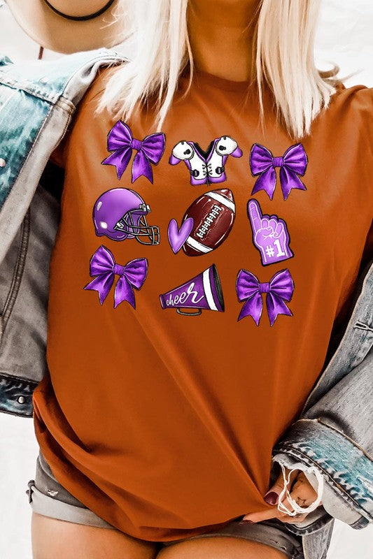 Someone wearing a Purple Coquette Football Graphic Tee, a unisex crew neck pink t-shirt decorated with sports-themed illustrations like a football, helmet, megaphone, foam finger, and cheerleading accessories in purple and white.