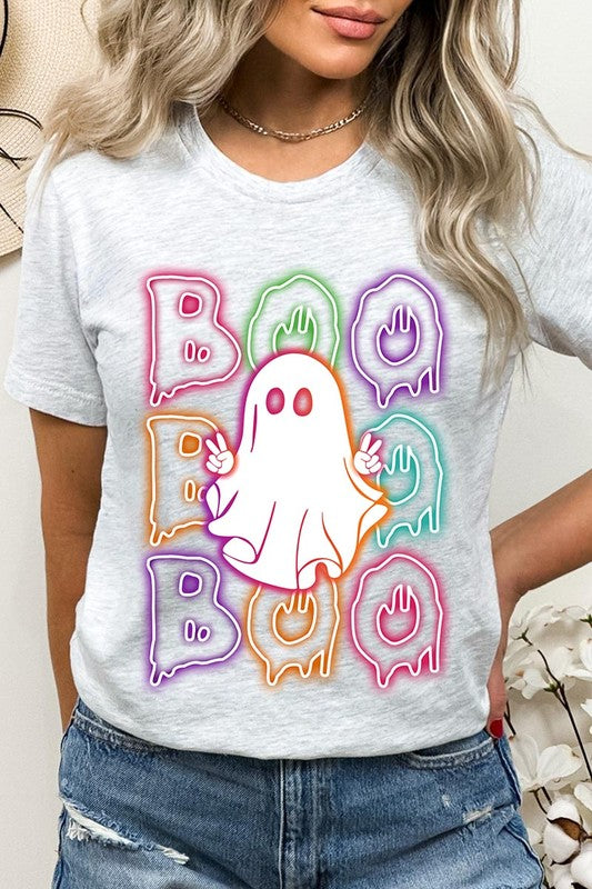 A person in a Boo Neon Halloween Ghost Graphic Tee, featuring neon letters spelling "BOO" with a cartoon ghost in the center. They are wearing light blue jeans and have a beige jacket draped over their arms.