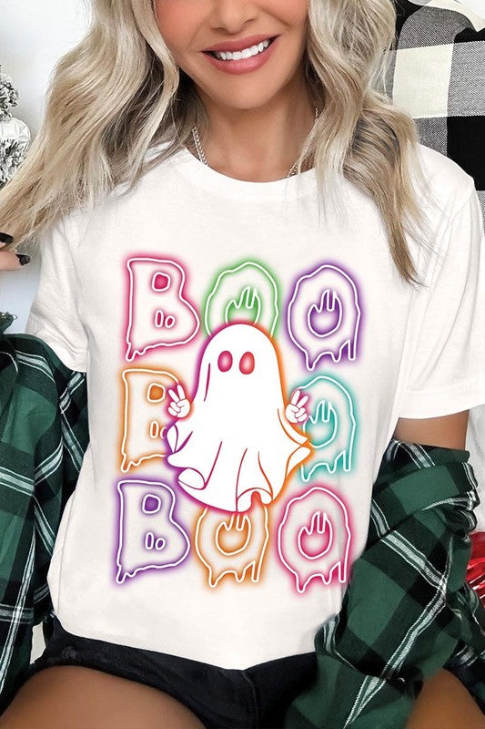 A person in a Boo Neon Halloween Ghost Graphic Tee, featuring neon letters spelling "BOO" with a cartoon ghost in the center. They are wearing light blue jeans and have a beige jacket draped over their arms.