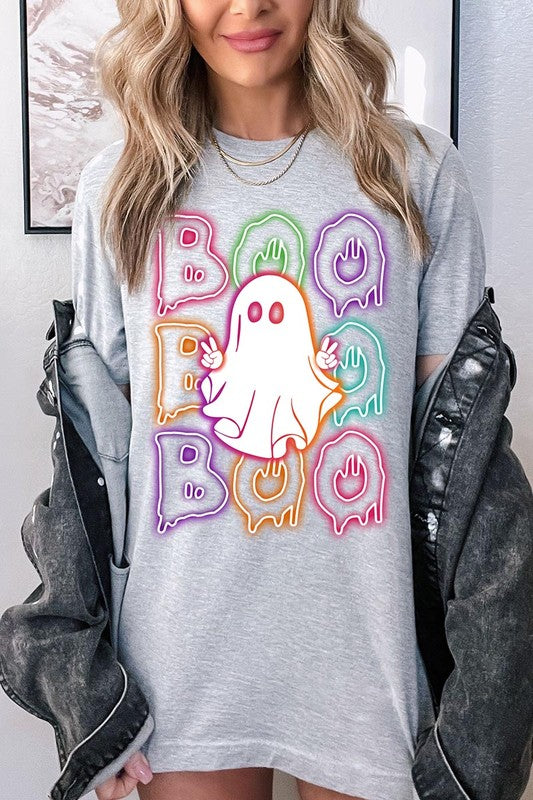 A person in a Boo Neon Halloween Ghost Graphic Tee, featuring neon letters spelling "BOO" with a cartoon ghost in the center. They are wearing light blue jeans and have a beige jacket draped over their arms.