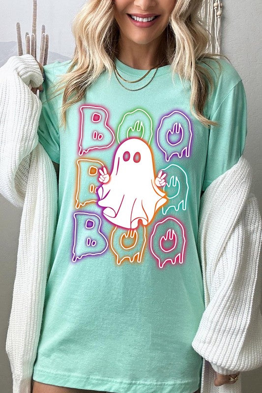 A person in a Boo Neon Halloween Ghost Graphic Tee, featuring neon letters spelling "BOO" with a cartoon ghost in the center. They are wearing light blue jeans and have a beige jacket draped over their arms.