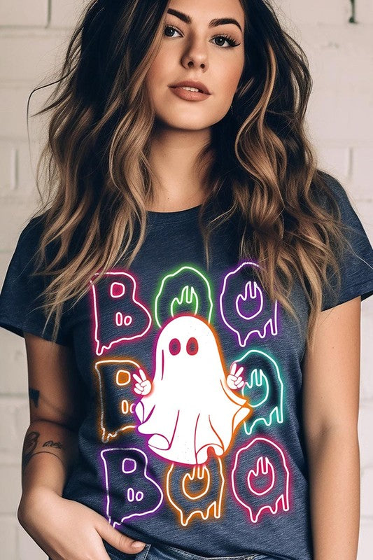 A person in a Boo Neon Halloween Ghost Graphic Tee, featuring neon letters spelling "BOO" with a cartoon ghost in the center. They are wearing light blue jeans and have a beige jacket draped over their arms.