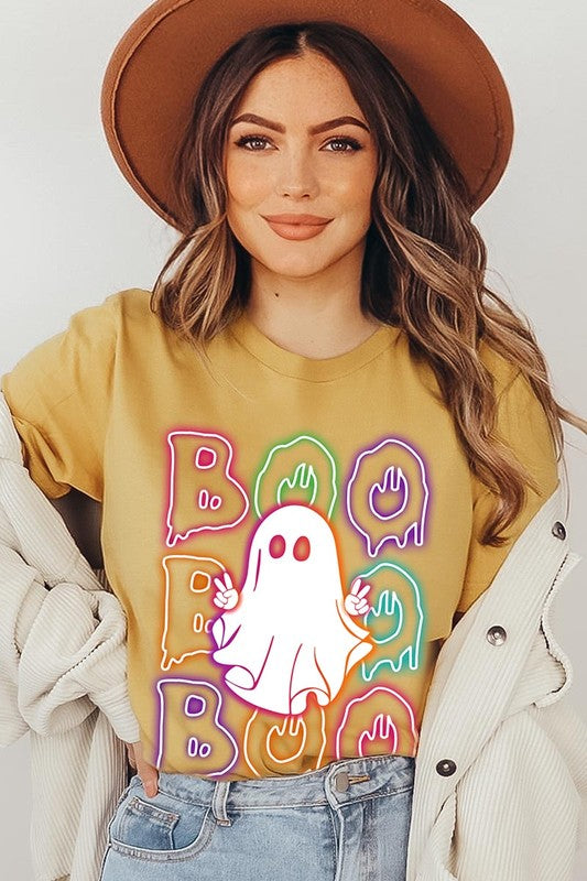 A person in a Boo Neon Halloween Ghost Graphic Tee, featuring neon letters spelling "BOO" with a cartoon ghost in the center. They are wearing light blue jeans and have a beige jacket draped over their arms.