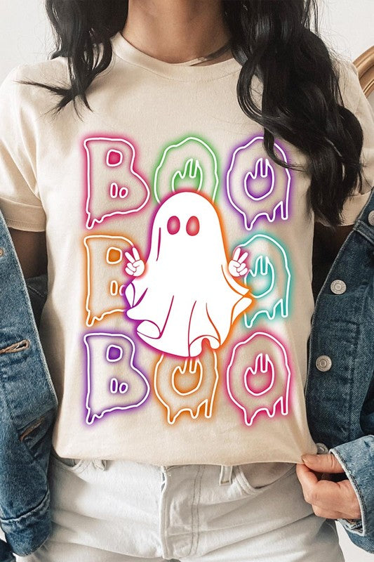 A person in a Boo Neon Halloween Ghost Graphic Tee, featuring neon letters spelling "BOO" with a cartoon ghost in the center. They are wearing light blue jeans and have a beige jacket draped over their arms.