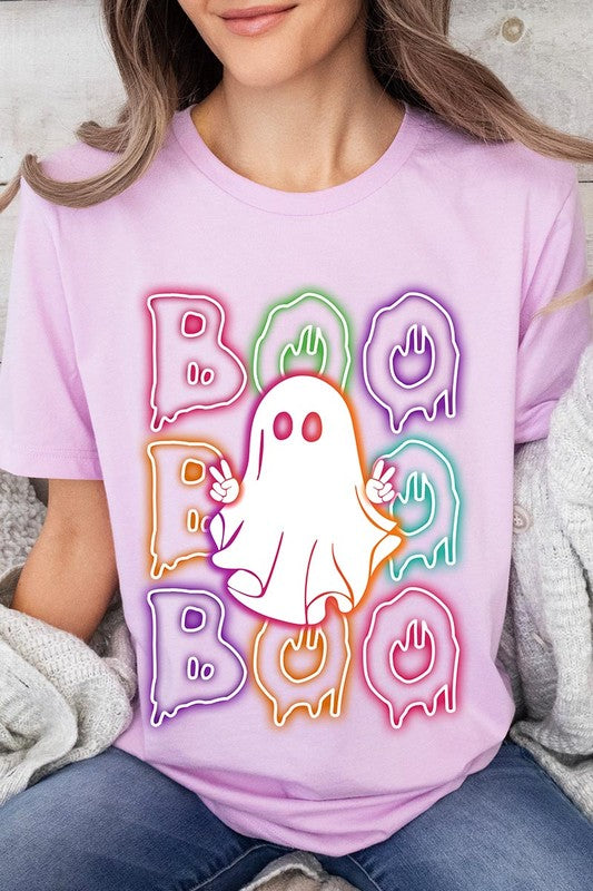 A person in a Boo Neon Halloween Ghost Graphic Tee, featuring neon letters spelling "BOO" with a cartoon ghost in the center. They are wearing light blue jeans and have a beige jacket draped over their arms.