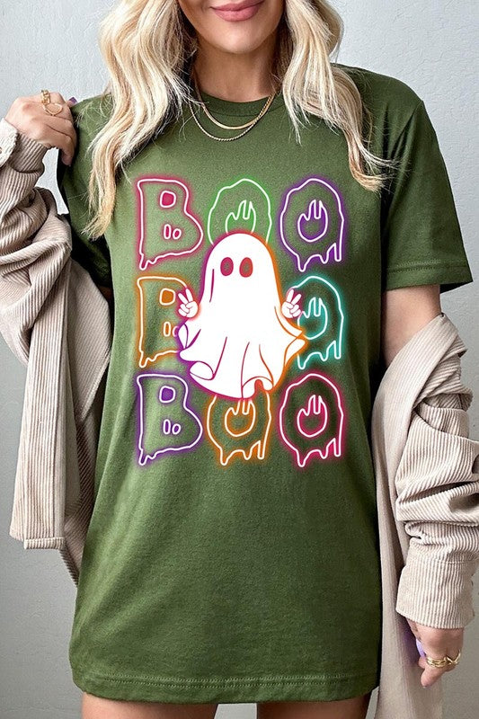 A person in a Boo Neon Halloween Ghost Graphic Tee, featuring neon letters spelling "BOO" with a cartoon ghost in the center. They are wearing light blue jeans and have a beige jacket draped over their arms.