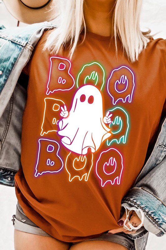 A person in a Boo Neon Halloween Ghost Graphic Tee, featuring neon letters spelling "BOO" with a cartoon ghost in the center. They are wearing light blue jeans and have a beige jacket draped over their arms.