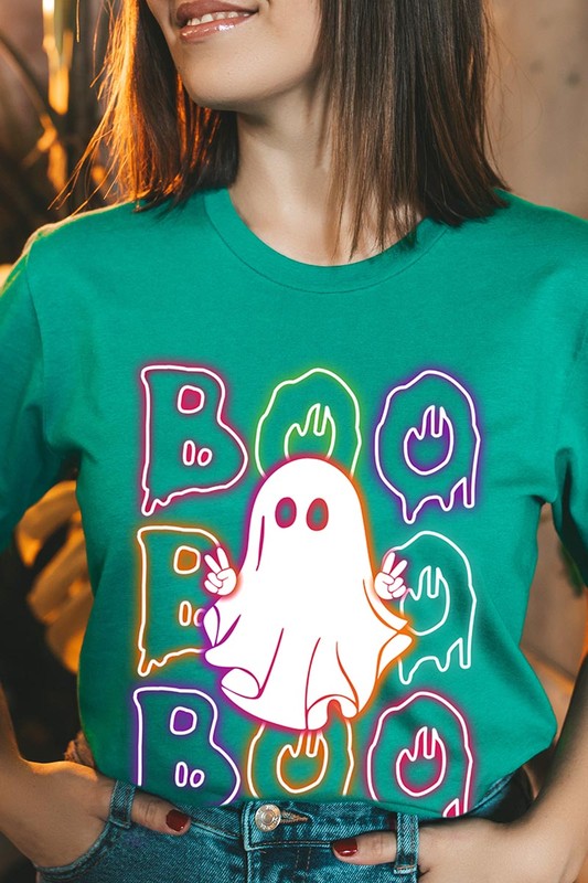 A person in a Boo Neon Halloween Ghost Graphic Tee, featuring neon letters spelling "BOO" with a cartoon ghost in the center. They are wearing light blue jeans and have a beige jacket draped over their arms.