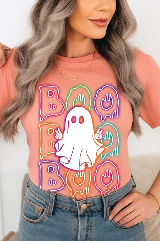 A person in a Boo Neon Halloween Ghost Graphic Tee, featuring neon letters spelling "BOO" with a cartoon ghost in the center. They are wearing light blue jeans and have a beige jacket draped over their arms.