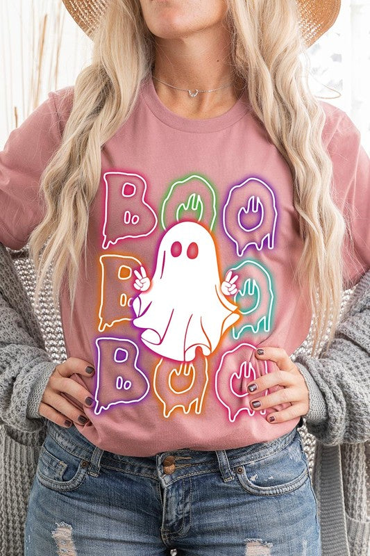 A person in a Boo Neon Halloween Ghost Graphic Tee, featuring neon letters spelling "BOO" with a cartoon ghost in the center. They are wearing light blue jeans and have a beige jacket draped over their arms.