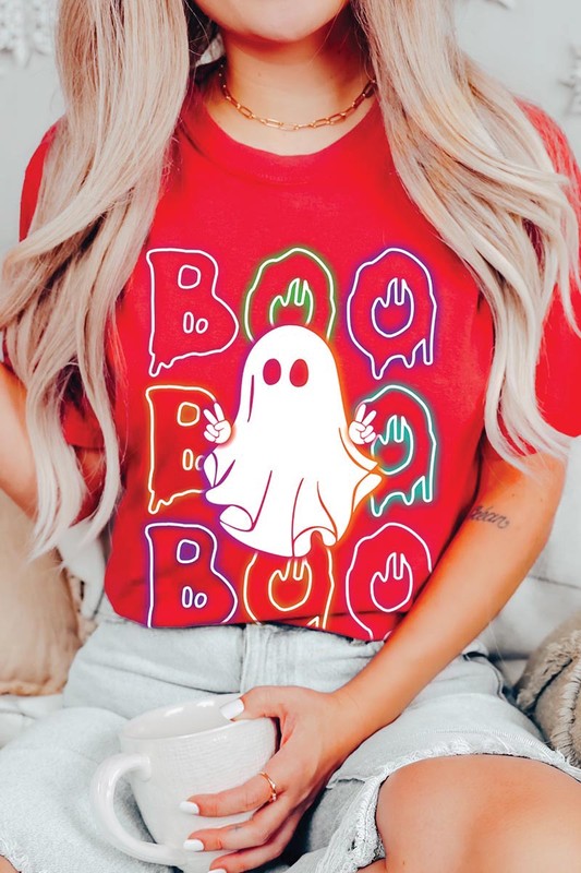 A person in a Boo Neon Halloween Ghost Graphic Tee, featuring neon letters spelling "BOO" with a cartoon ghost in the center. They are wearing light blue jeans and have a beige jacket draped over their arms.