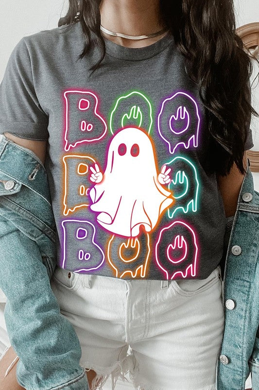 A person in a Boo Neon Halloween Ghost Graphic Tee, featuring neon letters spelling "BOO" with a cartoon ghost in the center. They are wearing light blue jeans and have a beige jacket draped over their arms.