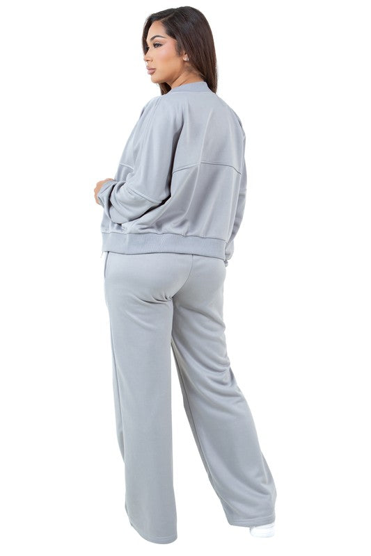 A person stands in a relaxed pose, wearing the WOMEN FASHION SWEATSUIT TWO PIECE PANT SET, which features a green zip-up jacket with a front-zip closure and matching green pants with an elasticized waist over a white top, paired with white sneakers.