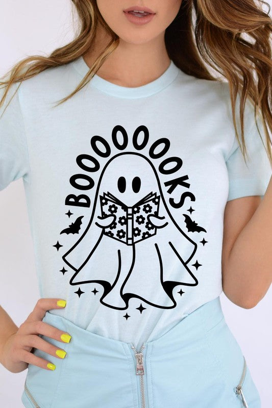 A person in a Cute Ghost Book Lover Graphic Tee featuring the text "BOOOOOOKS" holds a "Spells & Potions" book, set against a background of small bat decorations.