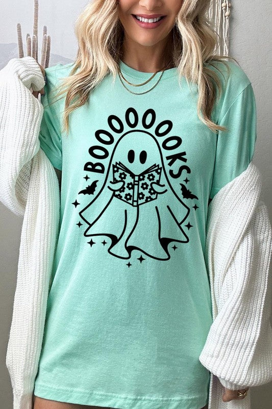 A person in a Cute Ghost Book Lover Graphic Tee featuring the text "BOOOOOOKS" holds a "Spells & Potions" book, set against a background of small bat decorations.