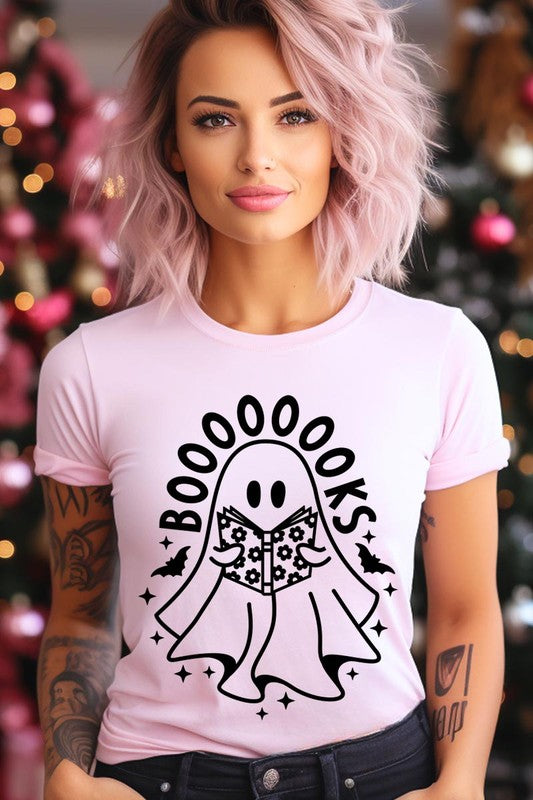 A person in a Cute Ghost Book Lover Graphic Tee featuring the text "BOOOOOOKS" holds a "Spells & Potions" book, set against a background of small bat decorations.