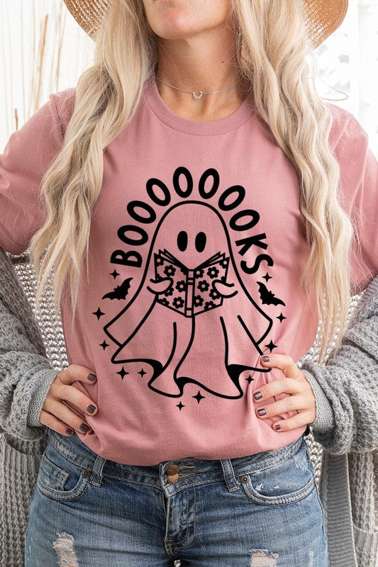 A person in a Cute Ghost Book Lover Graphic Tee featuring the text "BOOOOOOKS" holds a "Spells & Potions" book, set against a background of small bat decorations.