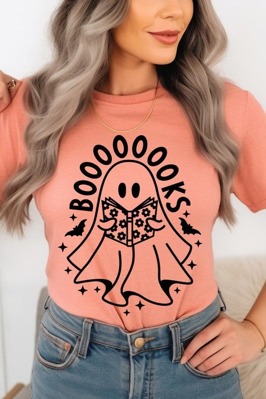 A person in a Cute Ghost Book Lover Graphic Tee featuring the text "BOOOOOOKS" holds a "Spells & Potions" book, set against a background of small bat decorations.