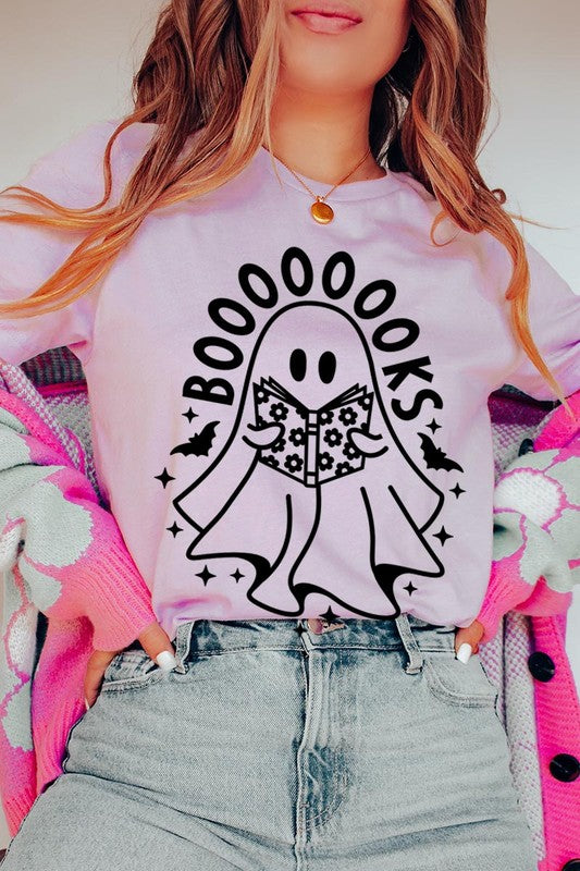 A person in a Cute Ghost Book Lover Graphic Tee featuring the text "BOOOOOOKS" holds a "Spells & Potions" book, set against a background of small bat decorations.