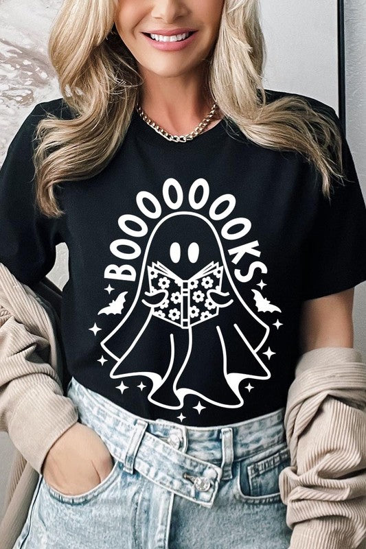 A person in a Cute Ghost Book Lover Graphic Tee featuring the text "BOOOOOOKS" holds a "Spells & Potions" book, set against a background of small bat decorations.