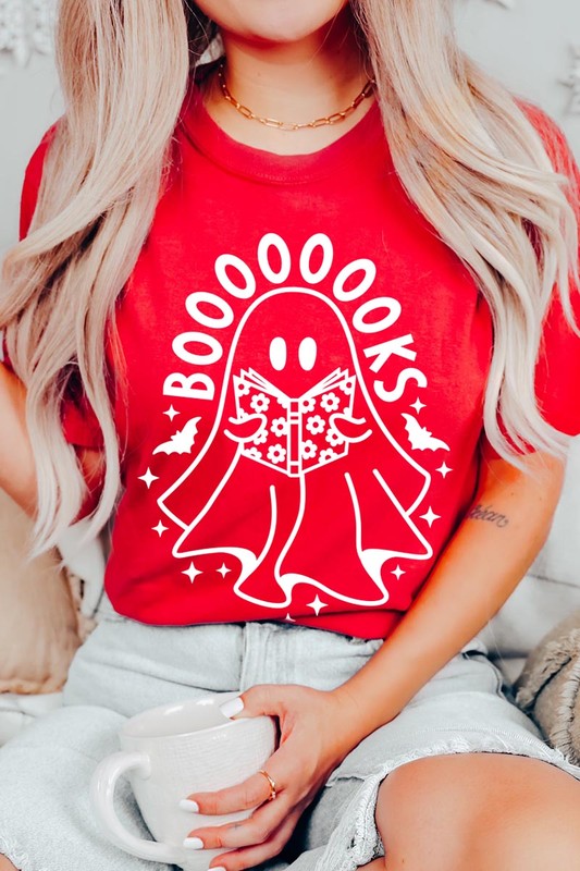 A person in a Cute Ghost Book Lover Graphic Tee featuring the text "BOOOOOOKS" holds a "Spells & Potions" book, set against a background of small bat decorations.