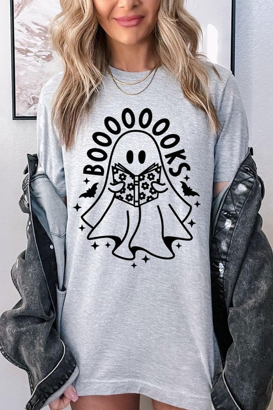 A person in a Cute Ghost Book Lover Graphic Tee featuring the text "BOOOOOOKS" holds a "Spells & Potions" book, set against a background of small bat decorations.