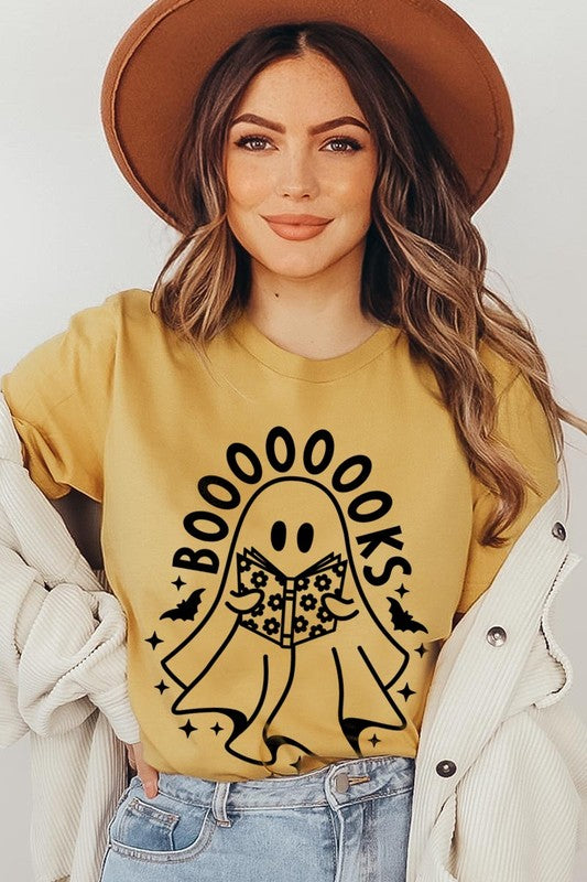 A person in a Cute Ghost Book Lover Graphic Tee featuring the text "BOOOOOOKS" holds a "Spells & Potions" book, set against a background of small bat decorations.