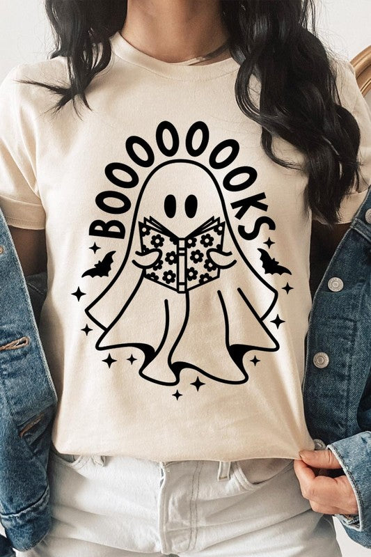 A person in a Cute Ghost Book Lover Graphic Tee featuring the text "BOOOOOOKS" holds a "Spells & Potions" book, set against a background of small bat decorations.