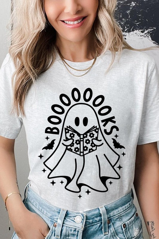 A person in a Cute Ghost Book Lover Graphic Tee featuring the text "BOOOOOOKS" holds a "Spells & Potions" book, set against a background of small bat decorations.