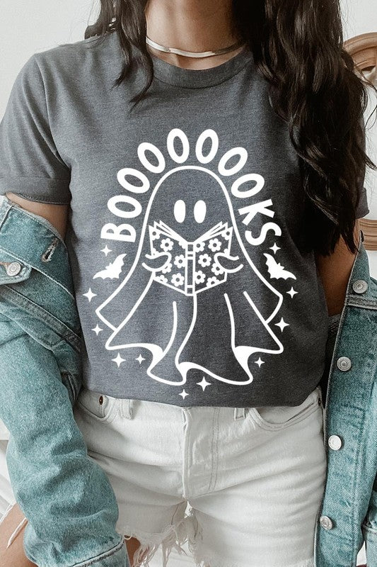 A person in a Cute Ghost Book Lover Graphic Tee featuring the text "BOOOOOOKS" holds a "Spells & Potions" book, set against a background of small bat decorations.