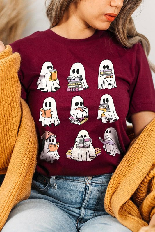 A person wears a brown shirt featuring illustrations of cute ghosts reading, holding, and interacting with books. This Funny Ghost Book Nerd Graphic Tee is paired with a partially worn denim jacket, showcasing its high-quality printed design.