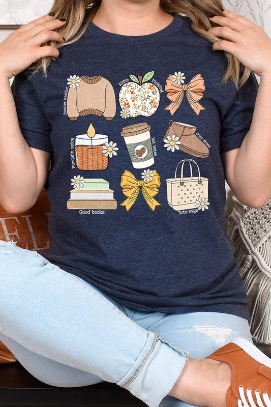 A person in a grey **Fall Girly Doodle Graphic Tee**, featuring charming illustrations of a sweater, apple, books, bows, coffee cup, candle, and tote bag, holds an orange mug while wearing a red cardigan and ripped jeans.