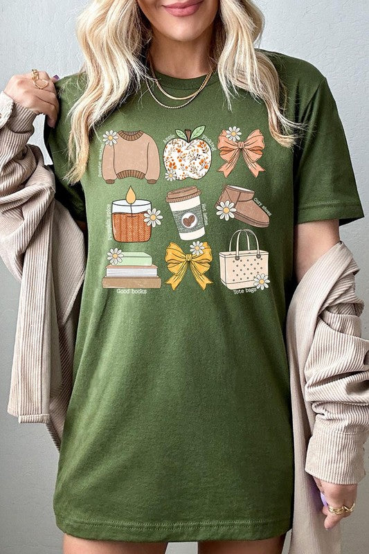 A person in a grey **Fall Girly Doodle Graphic Tee**, featuring charming illustrations of a sweater, apple, books, bows, coffee cup, candle, and tote bag, holds an orange mug while wearing a red cardigan and ripped jeans.