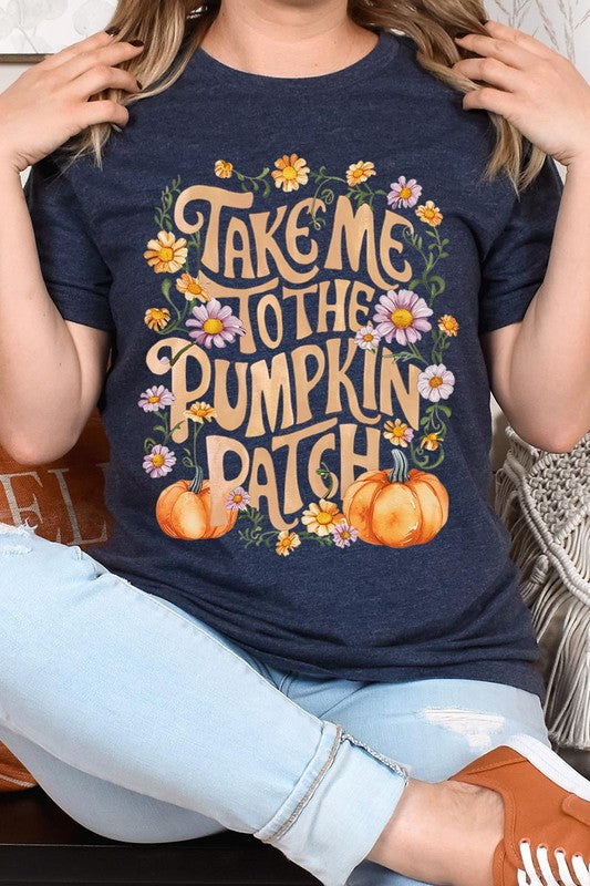 Person wearing a Take Me To The Pumpkin Patch Graphic Tee, which is a navy blue unisex crew neck t-shirt featuring the words "Take me to the pumpkin patch" surrounded by flowers and pumpkins.