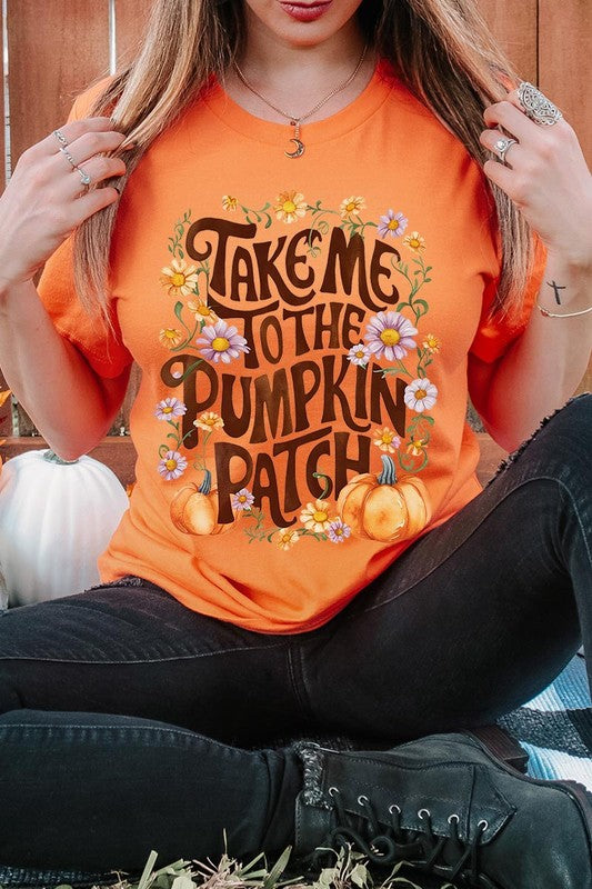 Person wearing a Take Me To The Pumpkin Patch Graphic Tee, which is a navy blue unisex crew neck t-shirt featuring the words "Take me to the pumpkin patch" surrounded by flowers and pumpkins.