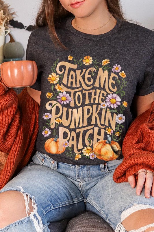 Person wearing a Take Me To The Pumpkin Patch Graphic Tee, which is a navy blue unisex crew neck t-shirt featuring the words "Take me to the pumpkin patch" surrounded by flowers and pumpkins.