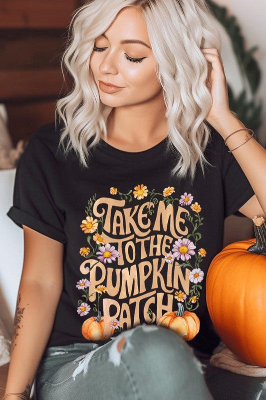 Person wearing a Take Me To The Pumpkin Patch Graphic Tee, which is a navy blue unisex crew neck t-shirt featuring the words "Take me to the pumpkin patch" surrounded by flowers and pumpkins.