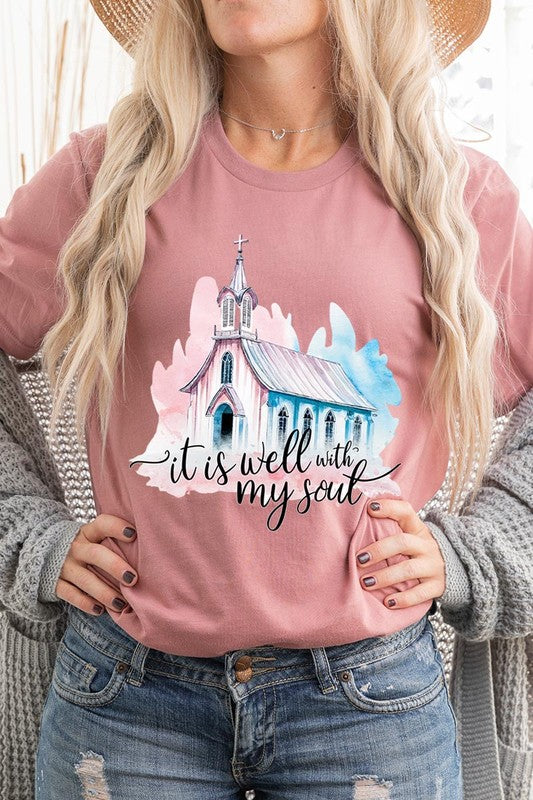 A woman wearing the "It Is Well With My Soul" graphic tee, featuring a grey color with an illustration of a church and the text "it is well with my soul.