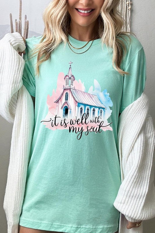 A woman wearing the "It Is Well With My Soul" graphic tee, featuring a grey color with an illustration of a church and the text "it is well with my soul.